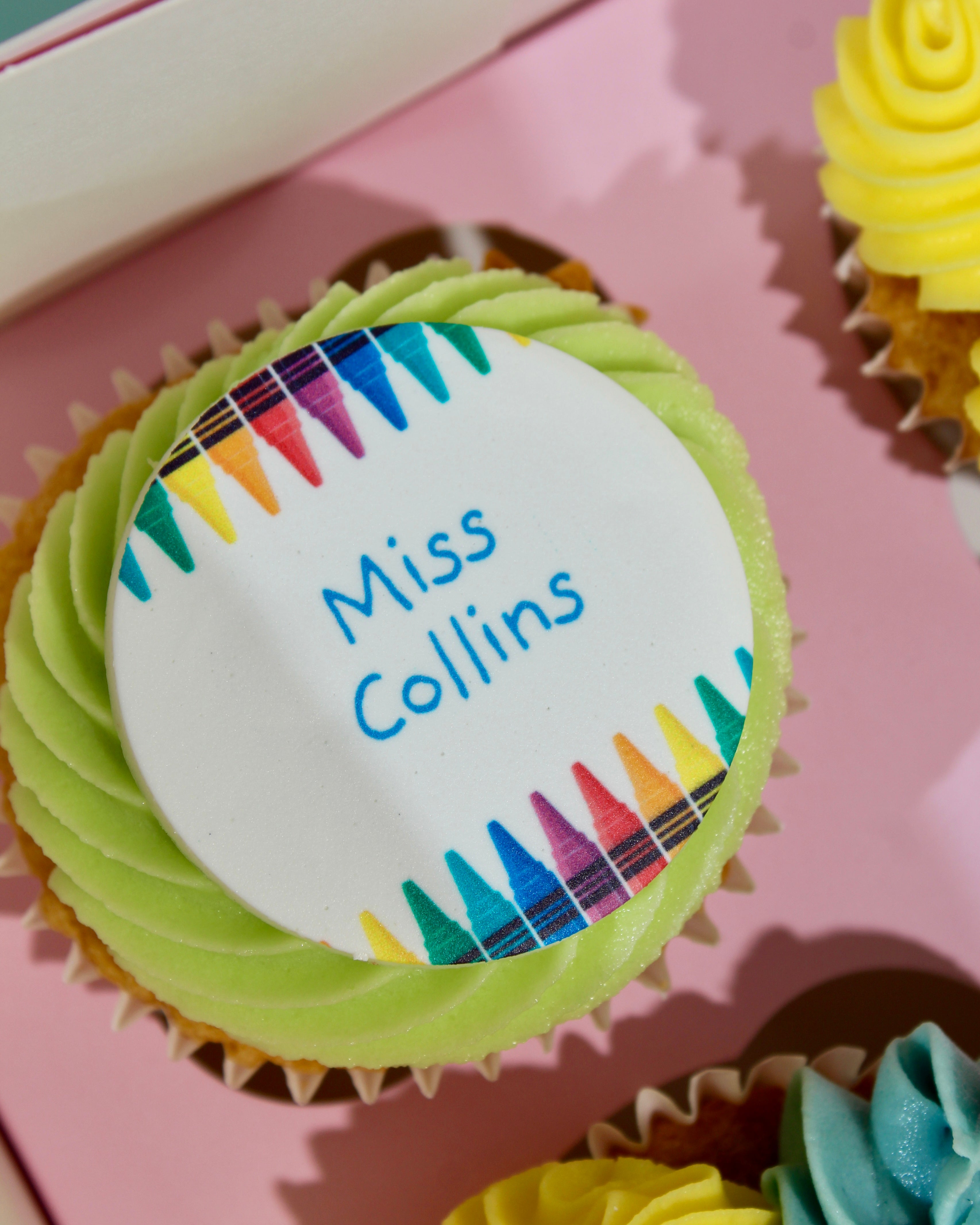 Close-up of personalised teacher name cupcake disc with rainbow crayon border reading Miss Collins

