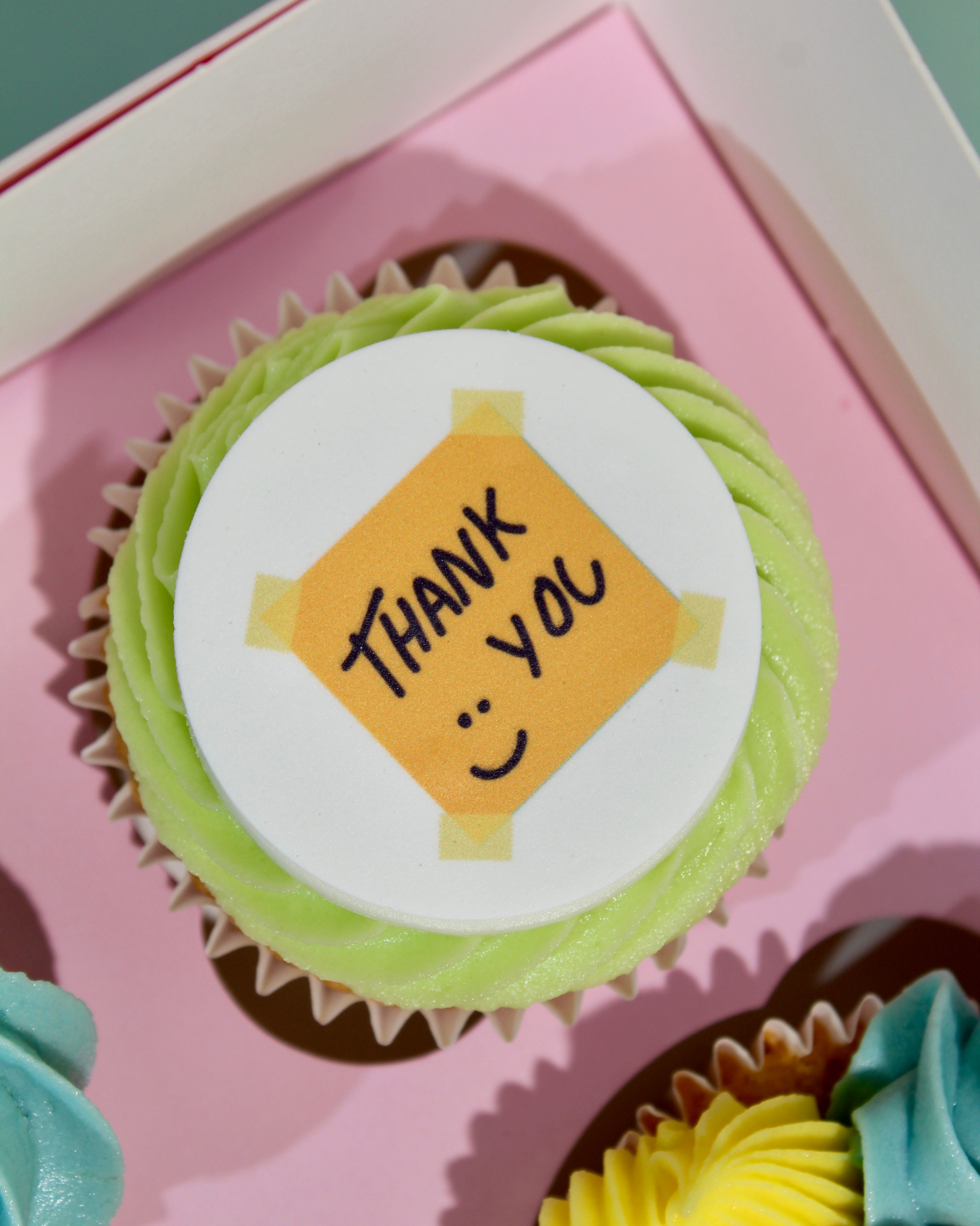 Close-up of Thank You teacher cupcake with sticky note disc and green buttercream rosette in pink gift box