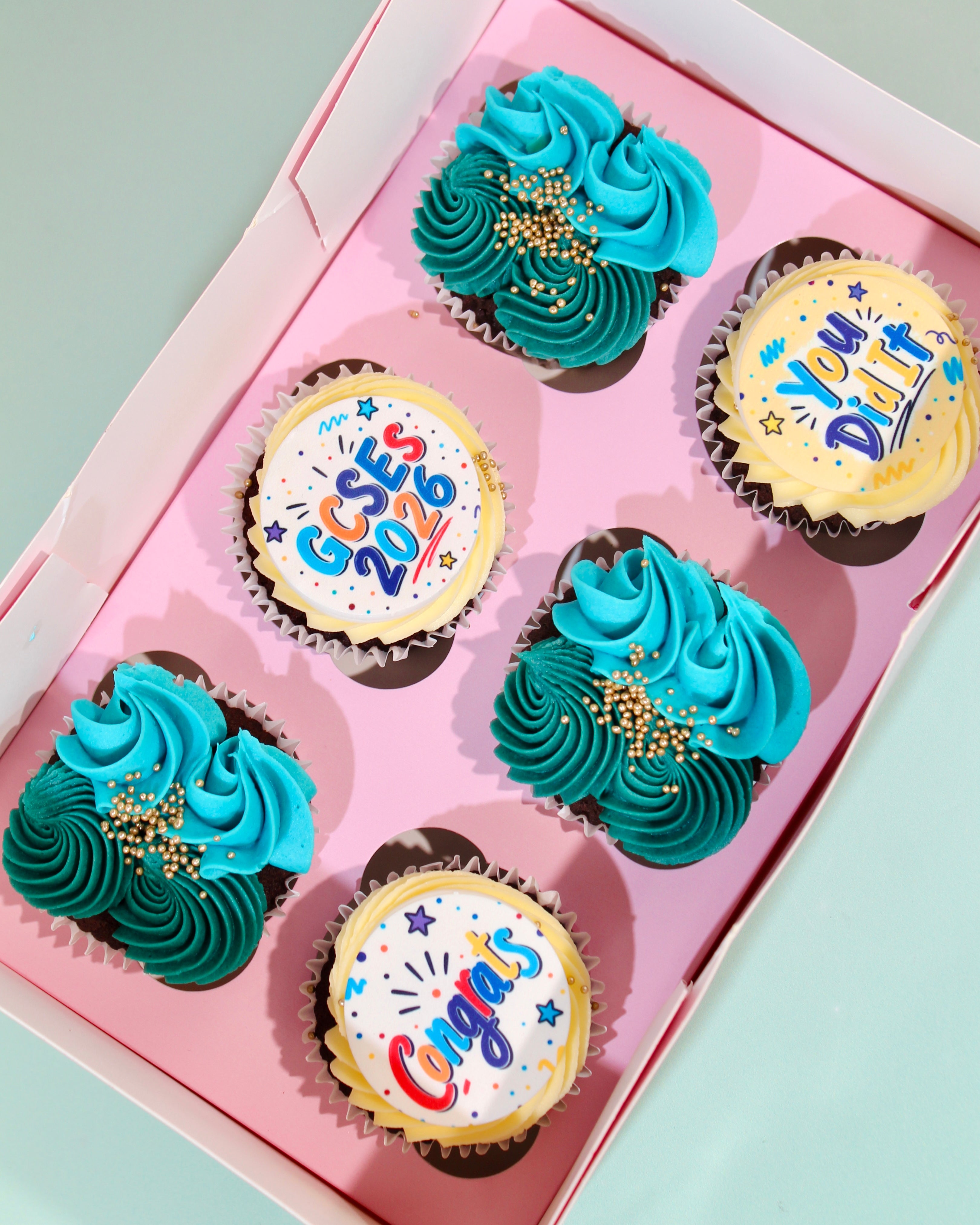 Box of six GCSE 2026 cupcakes with GCSEs 2026 disc, You Did It and Congrats designs in teal and blue buttercream