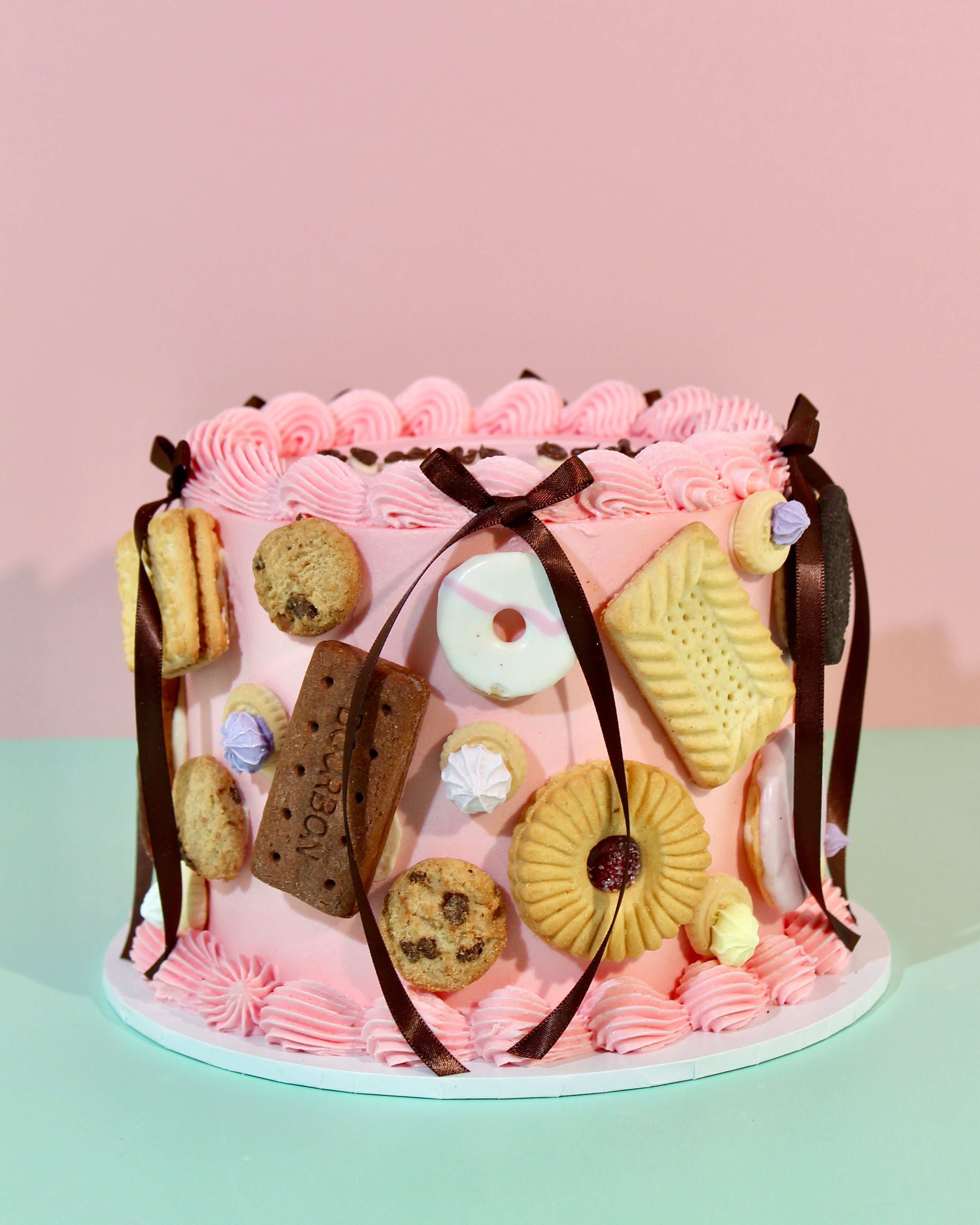  Pink buttercream birthday cake covered in real biscuits including Bourbons, Jammie Dodgers and Party Rings with chocolate ribbon bows
