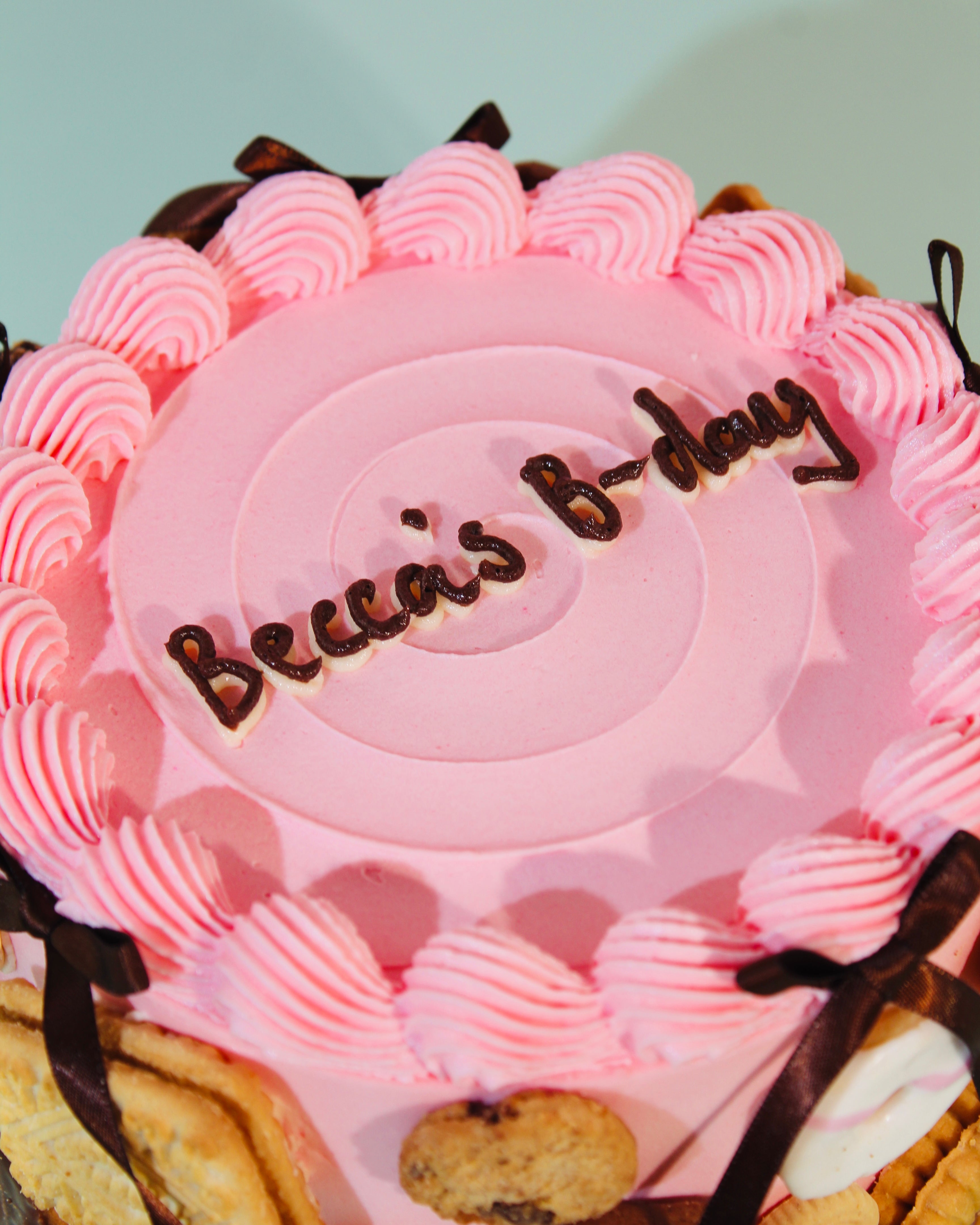 Top-down view of Biscuit Cake showing personalised iced message and pink piped buttercream border with biscuit decorations
