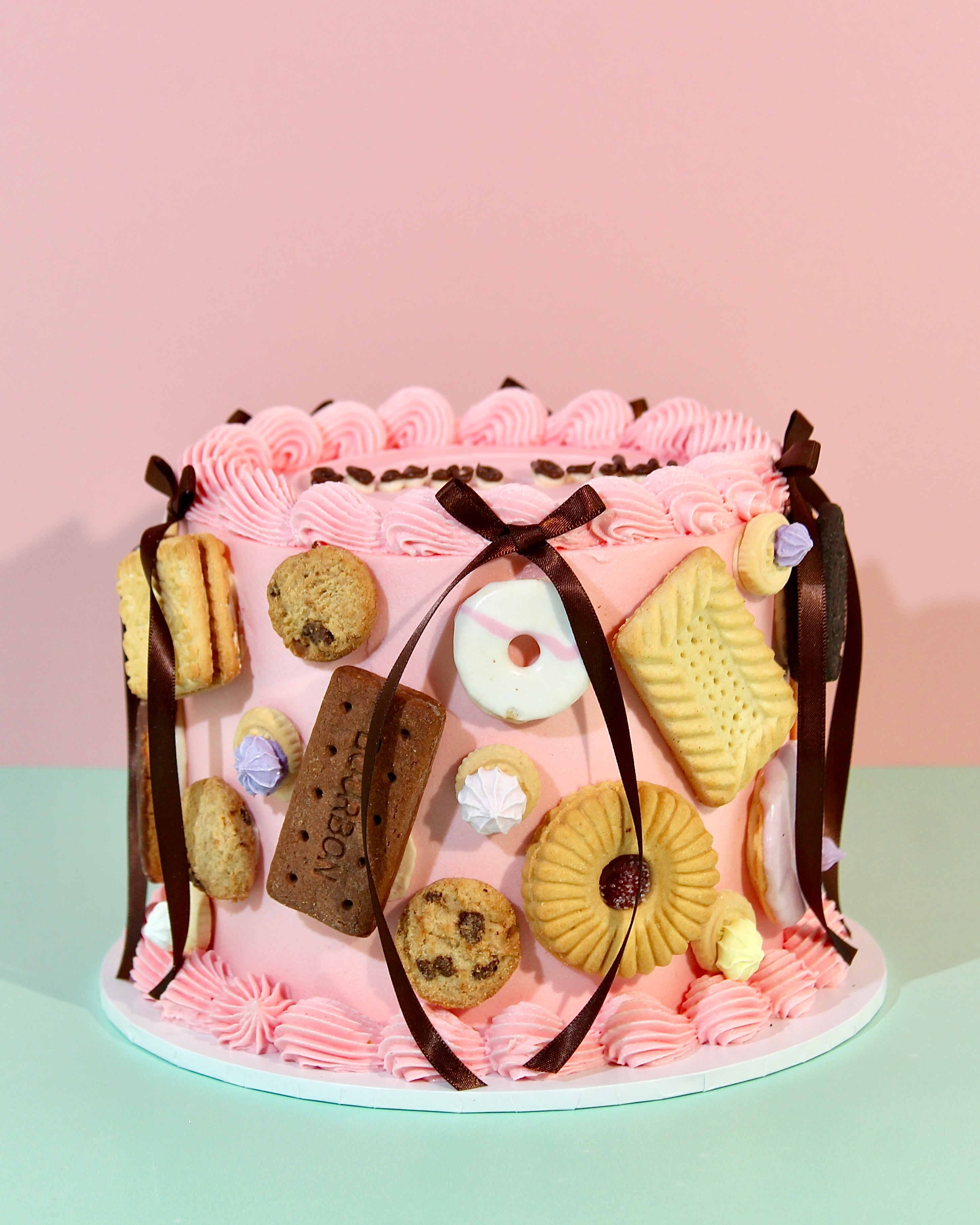 Close-up of Biscuit Cake showing Bourbon, Party Ring, Custard Cream and chocolate chip cookie decorations on pink buttercream