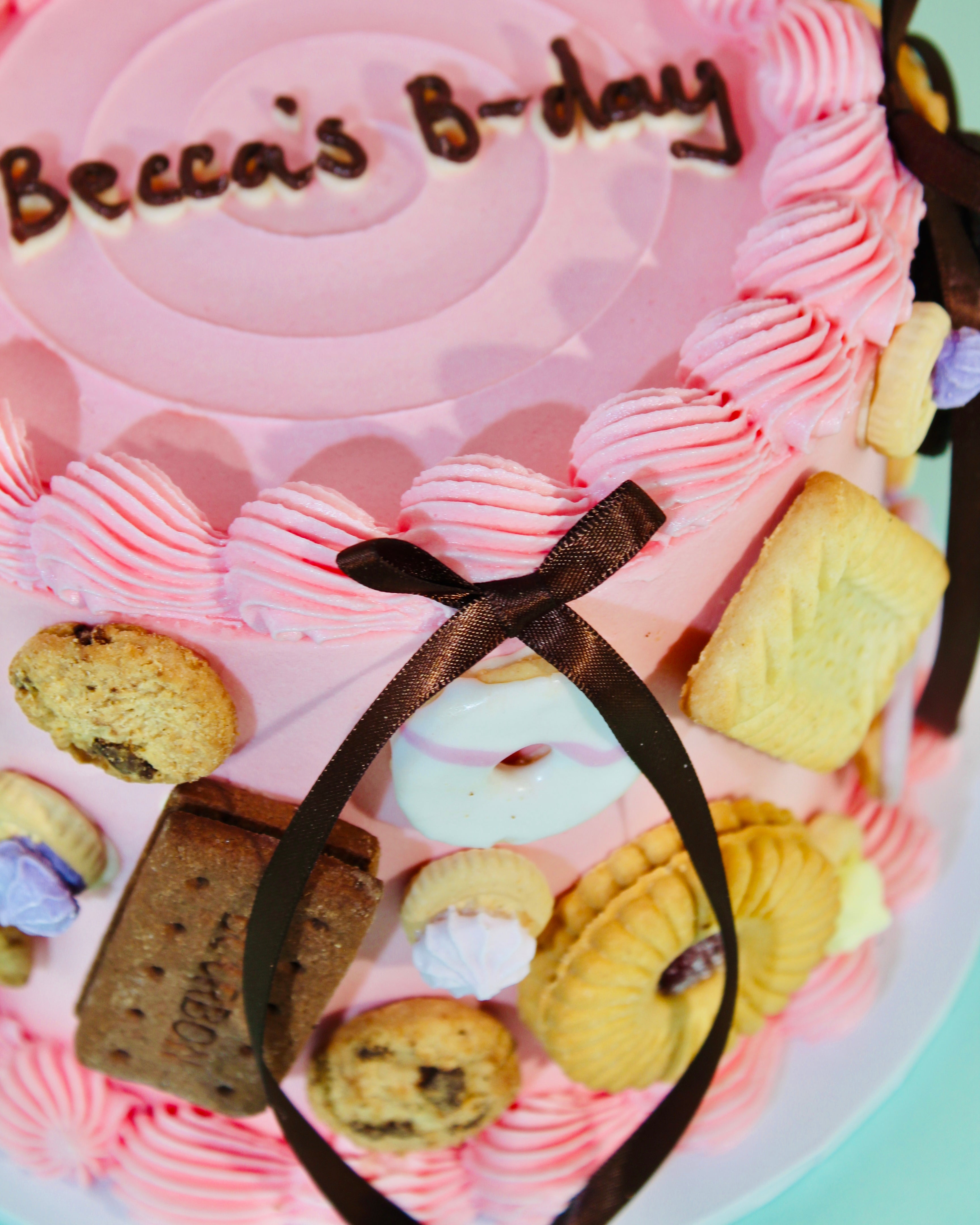 Detail shot of real biscuits and chocolate satin ribbon bow on pink personalised birthday cake