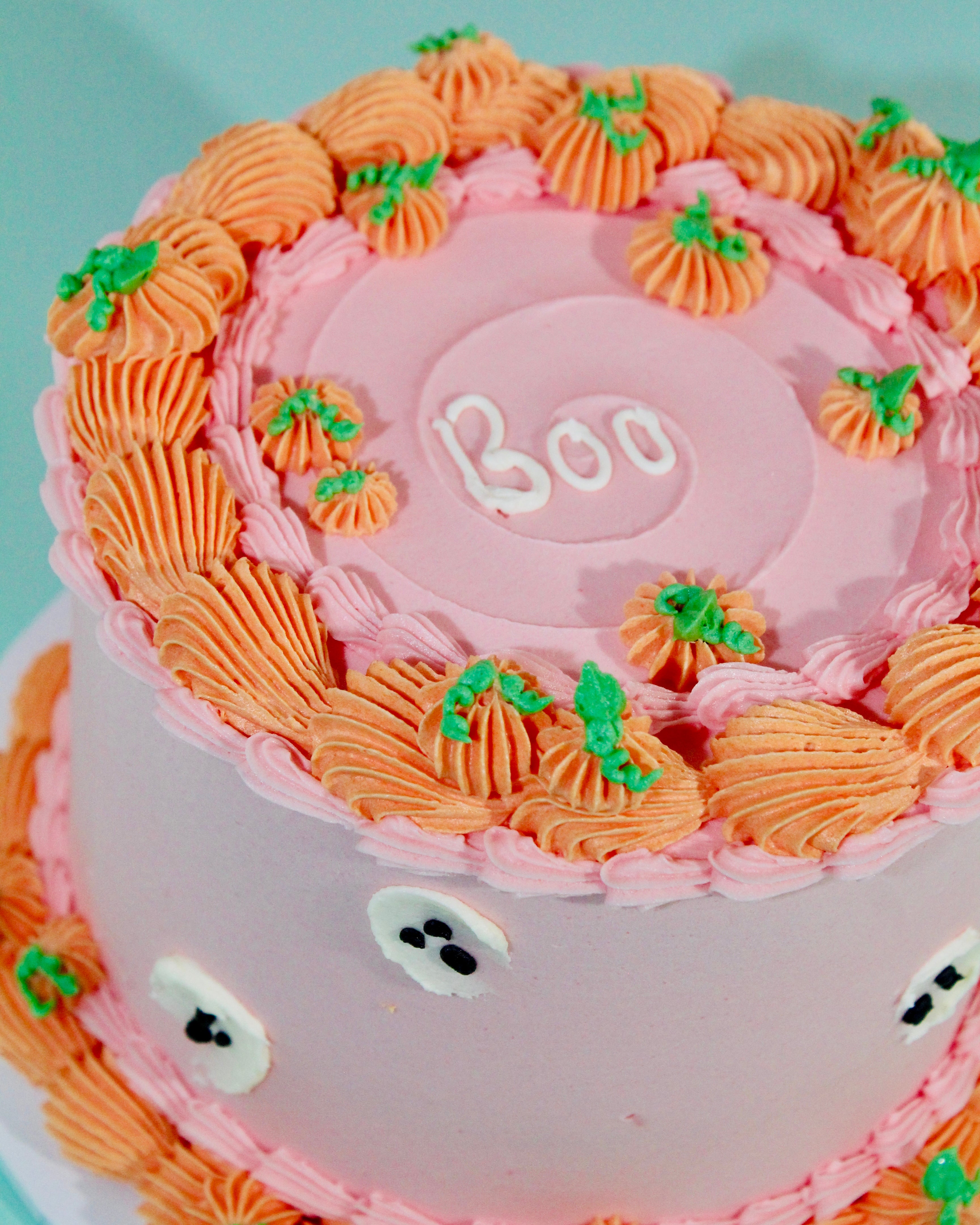 Pink Halloween pumpkin cake with hand-piped orange pumpkin rosettes, ghost details and Boo message on top