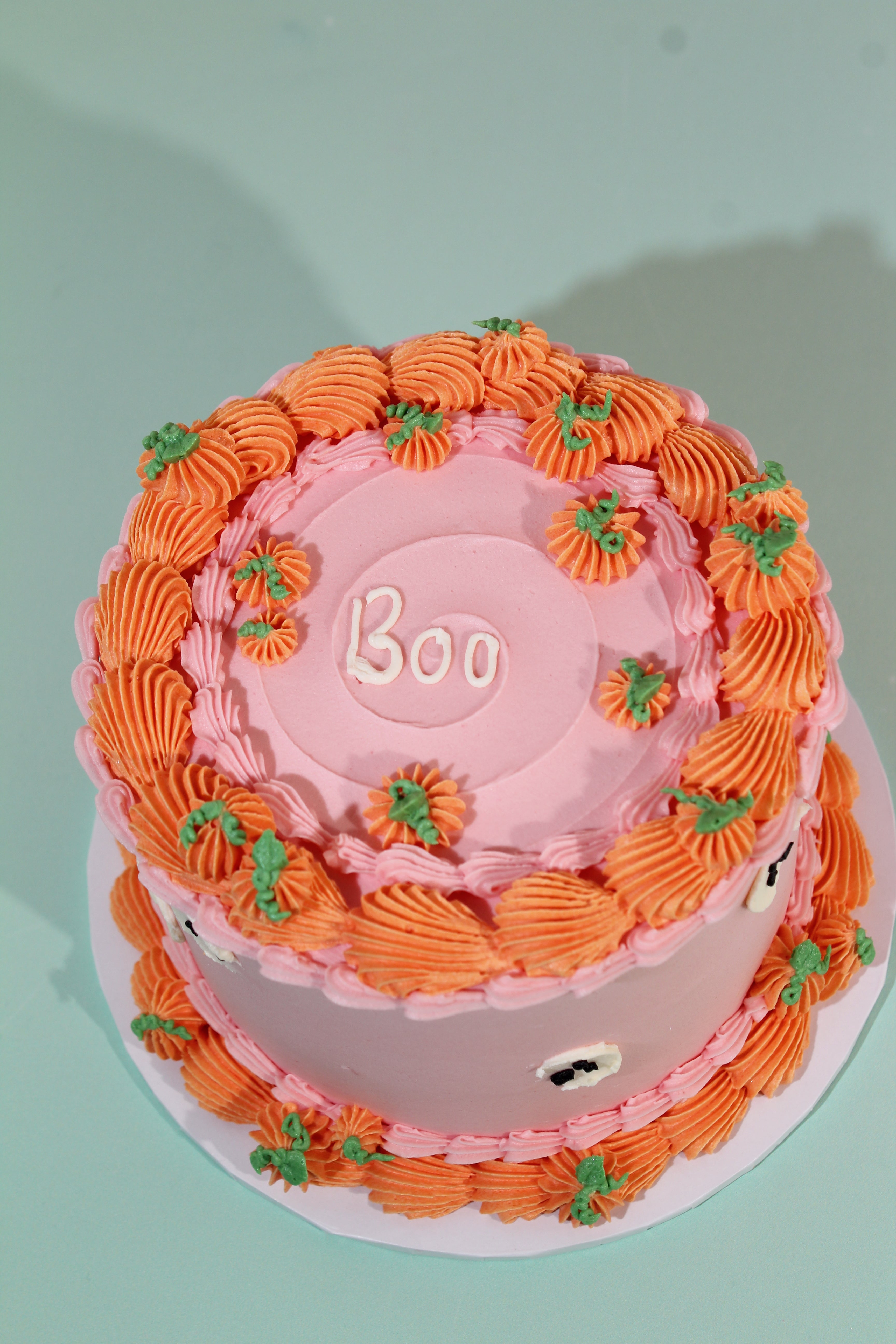 Close-up of hand-piped orange buttercream pumpkin rosettes with green leaf detail on pink Halloween cake
