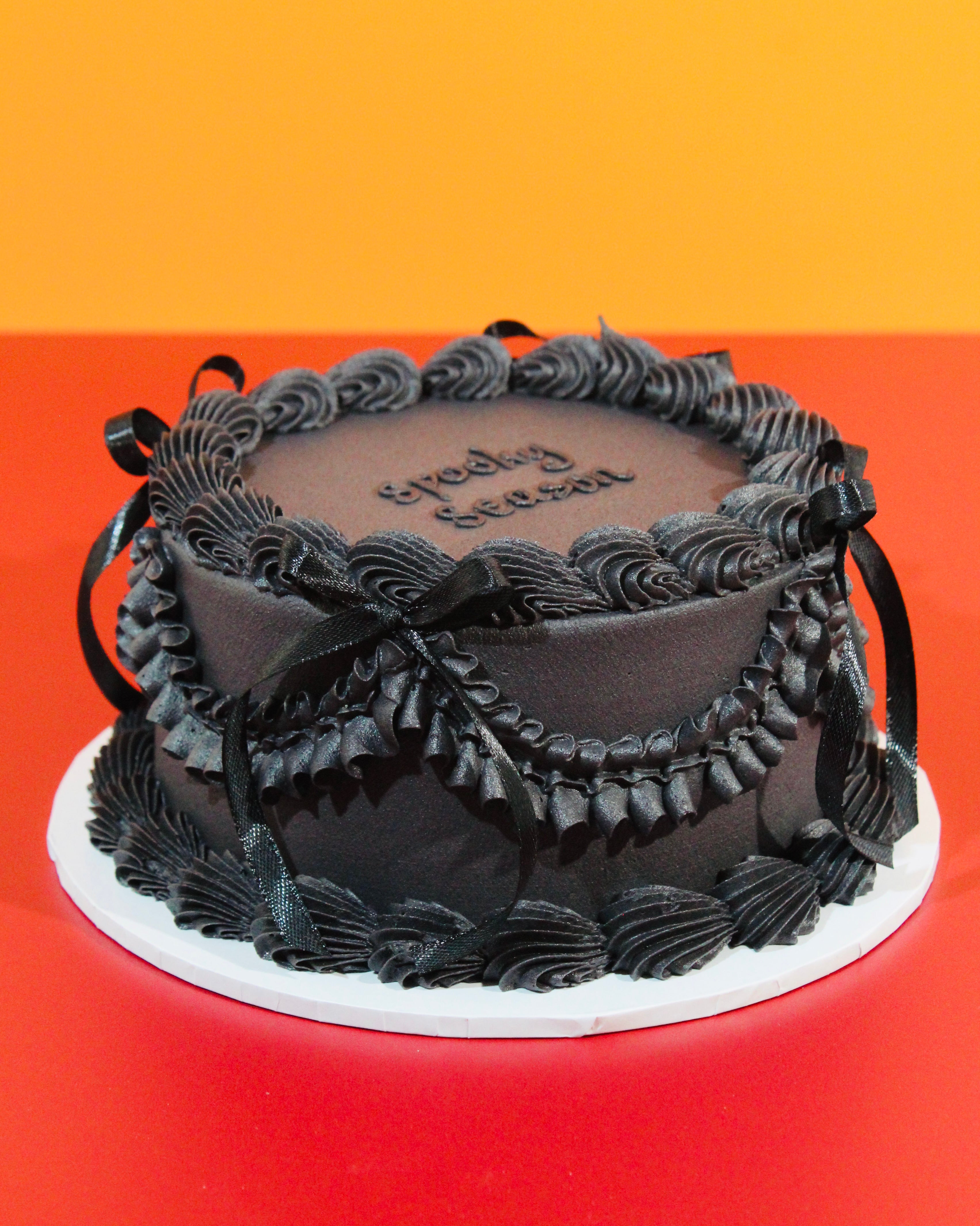 Elegant black Midnight Halloween cake with gothic piped buttercream detailing and black satin ribbon bows on red background