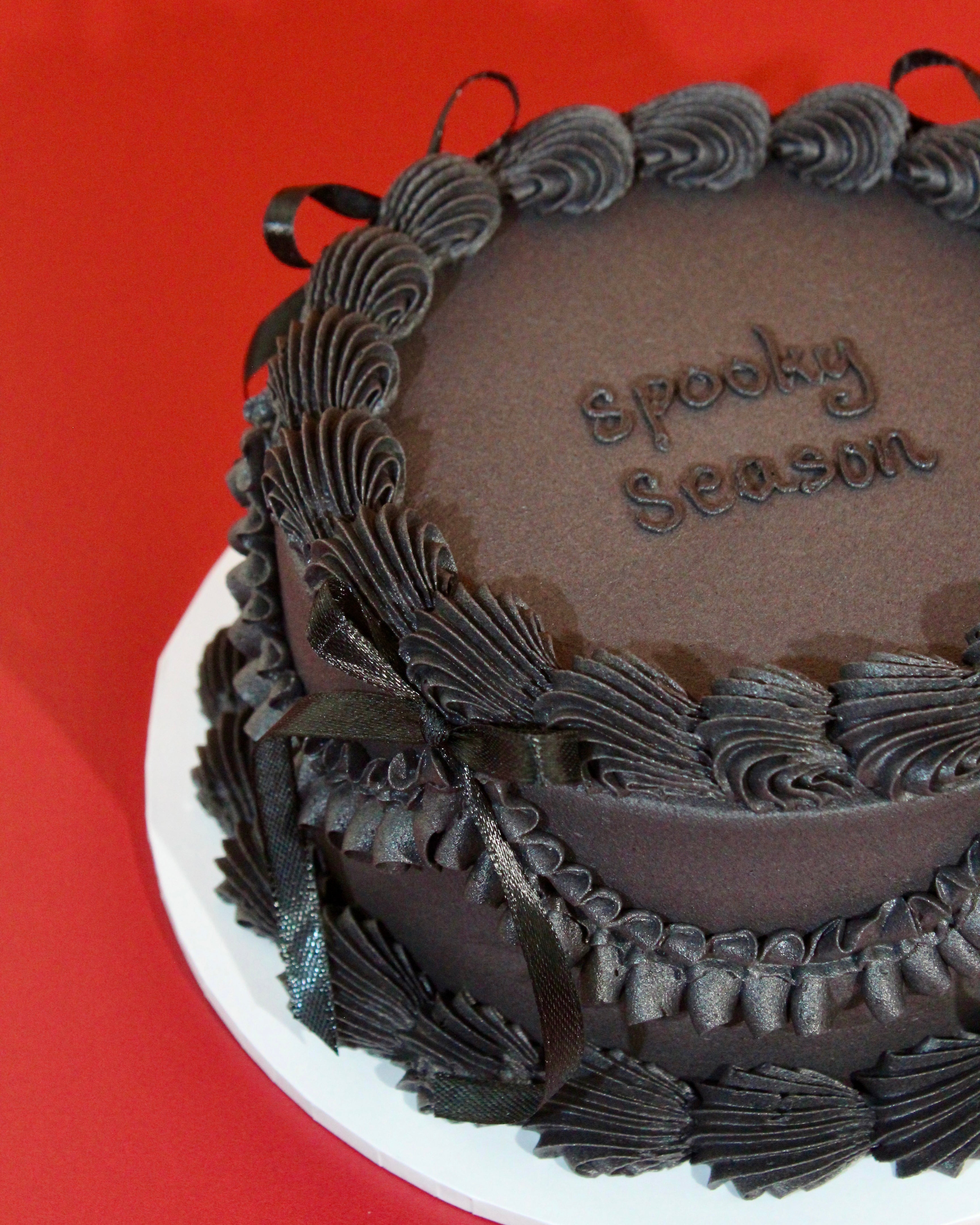 Bird's eye view of black Halloween cake showing personalised iced message surrounded by intricate piped buttercream border