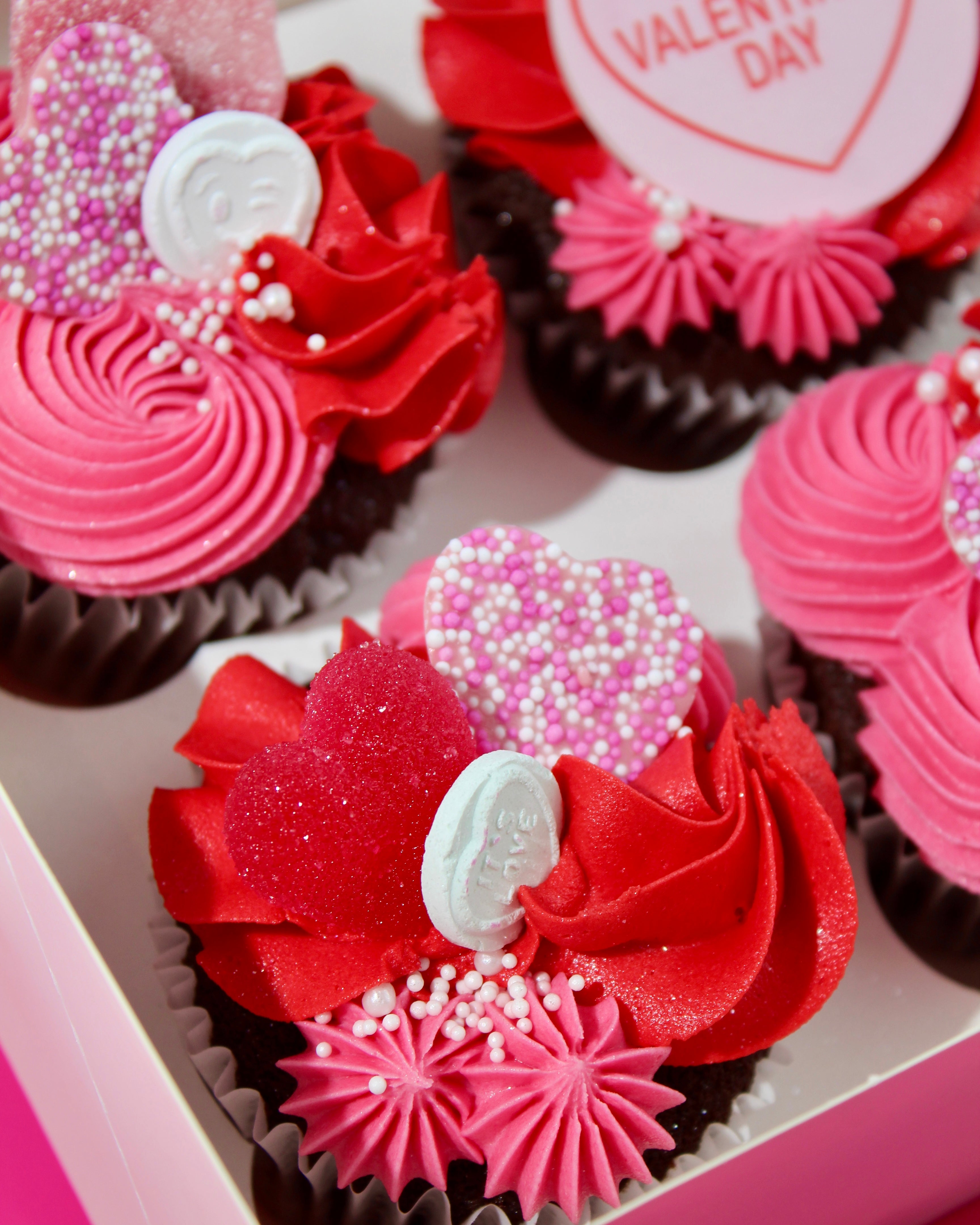 Pink and red Galentine’s cupcakes arranged in a white bakery box