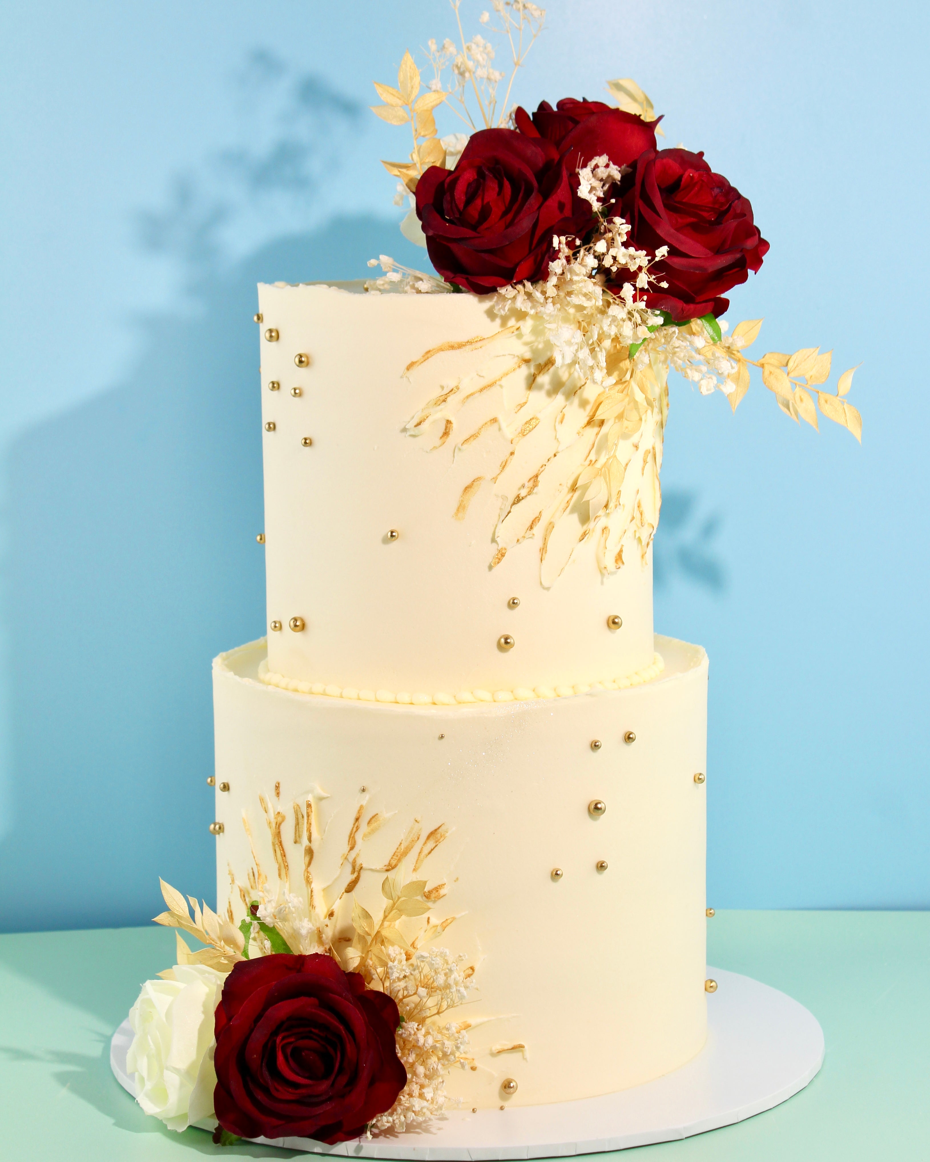 Luxury ivory wedding cake with gold detailing and deep red rose florals