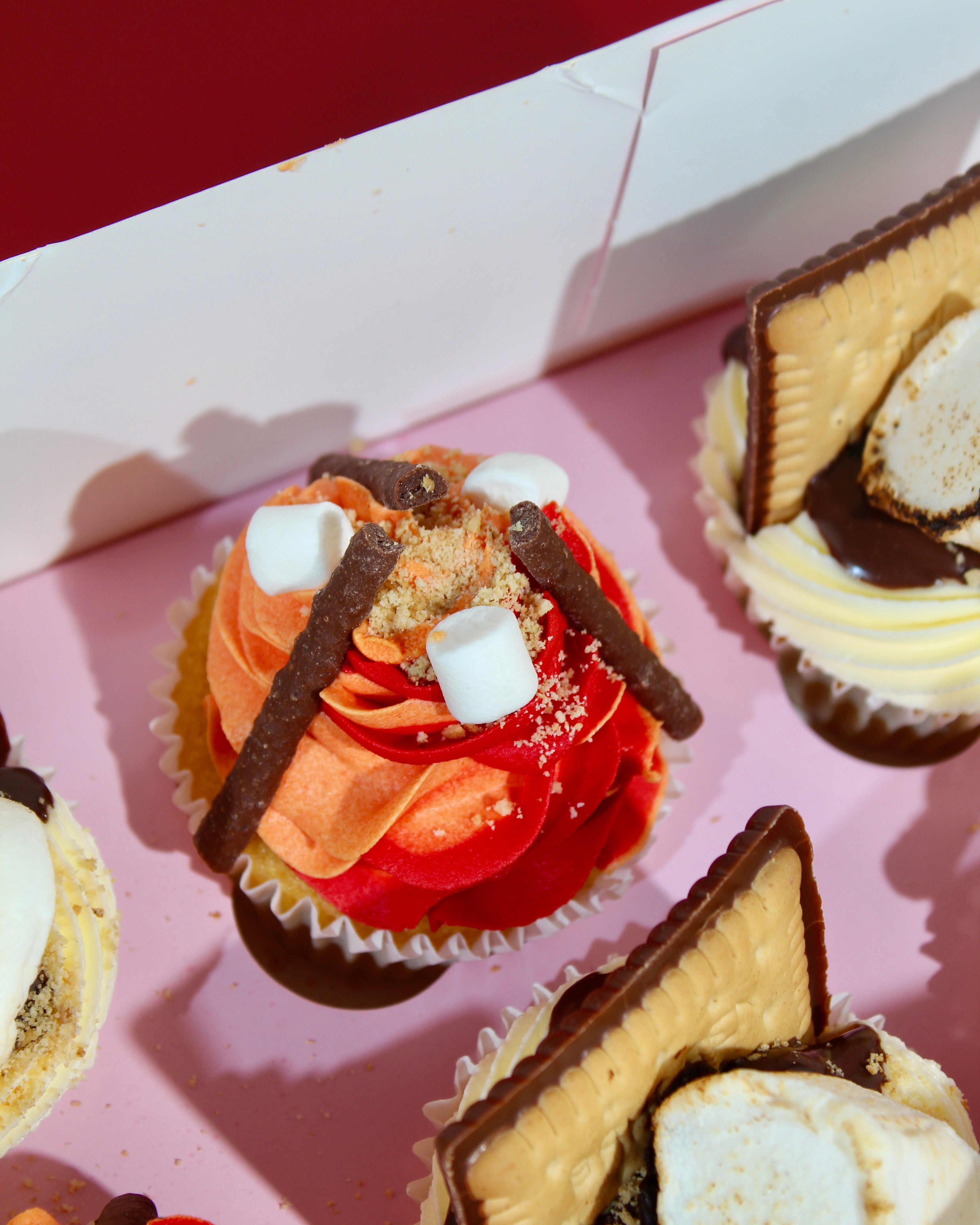Close-up of orange and red two-tone rosette Bonfire Night cupcake with chocolate sticks, mini marshmallows and biscuit crumble