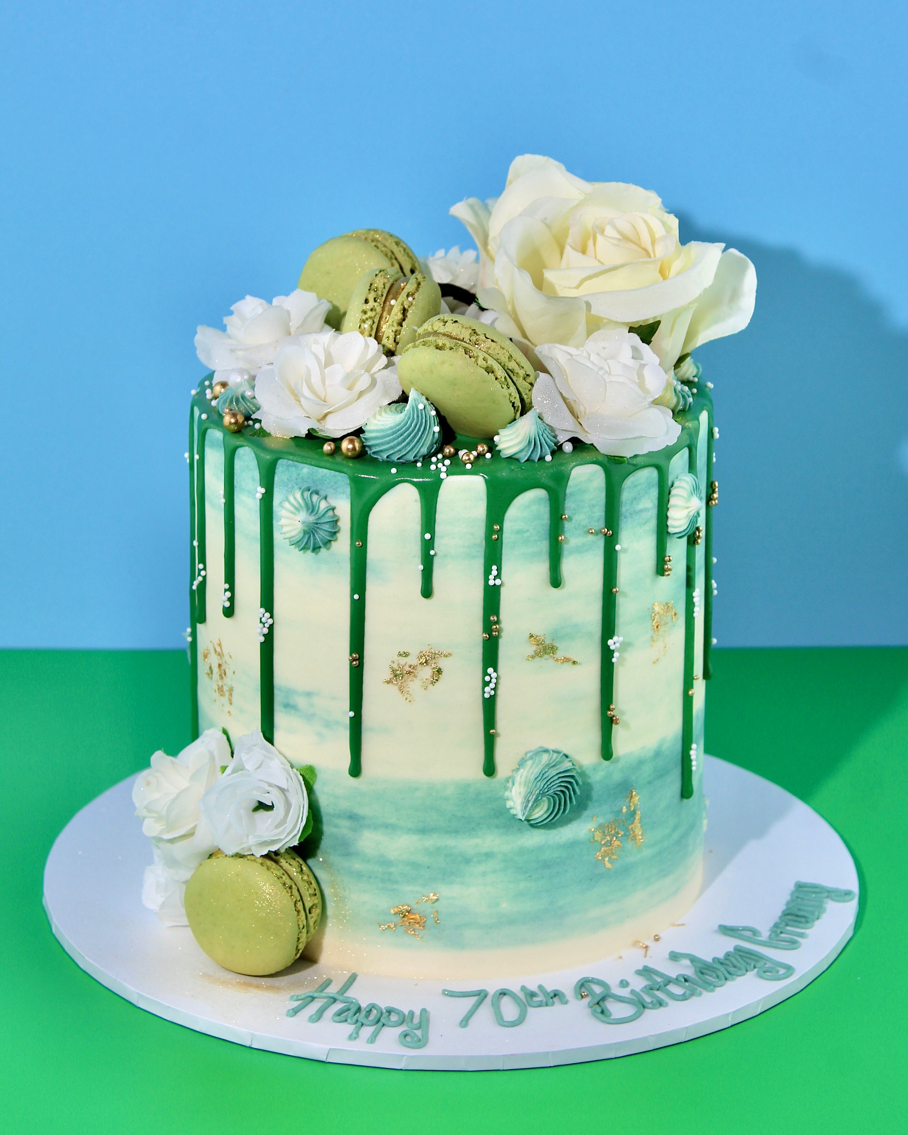 Elegant green drip birthday cake with white roses, macarons and gold leaf decoration