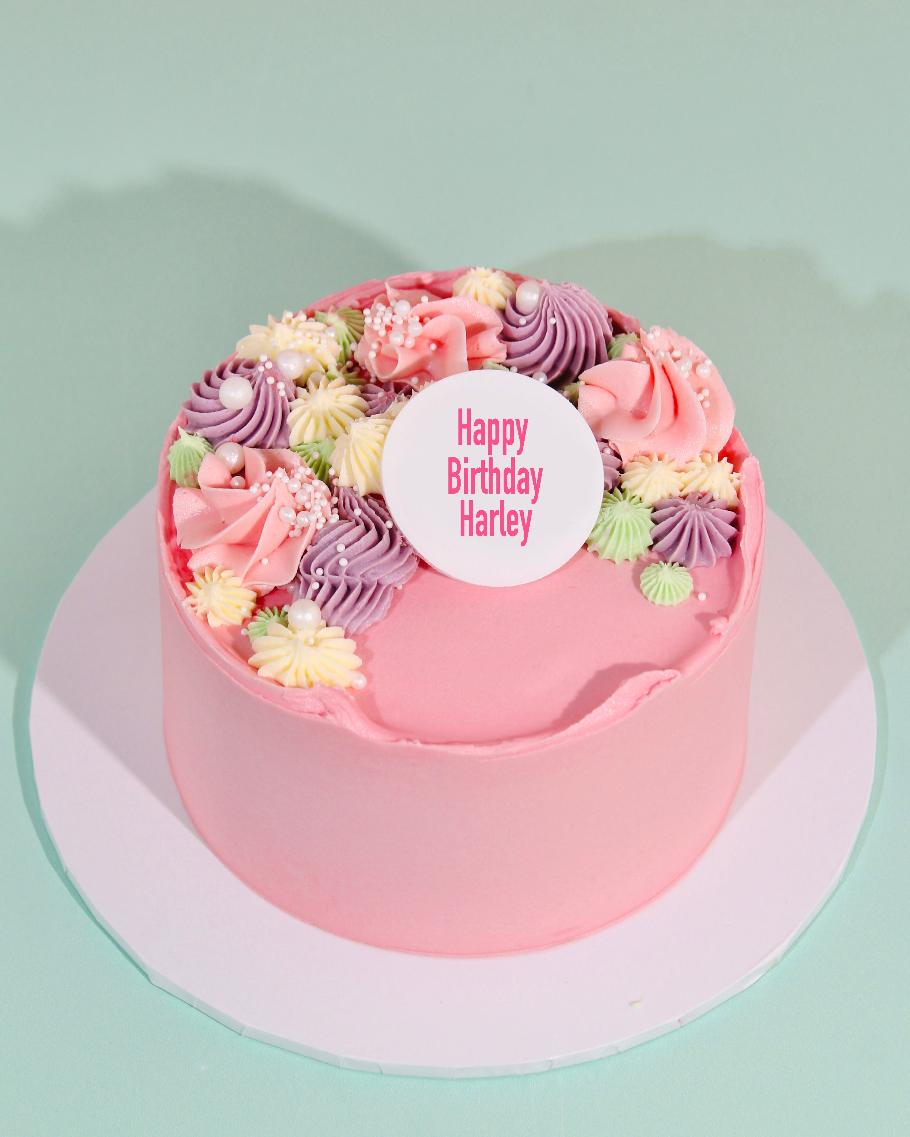Pink birthday cake with floral decorations and a personalized tag on a light green background