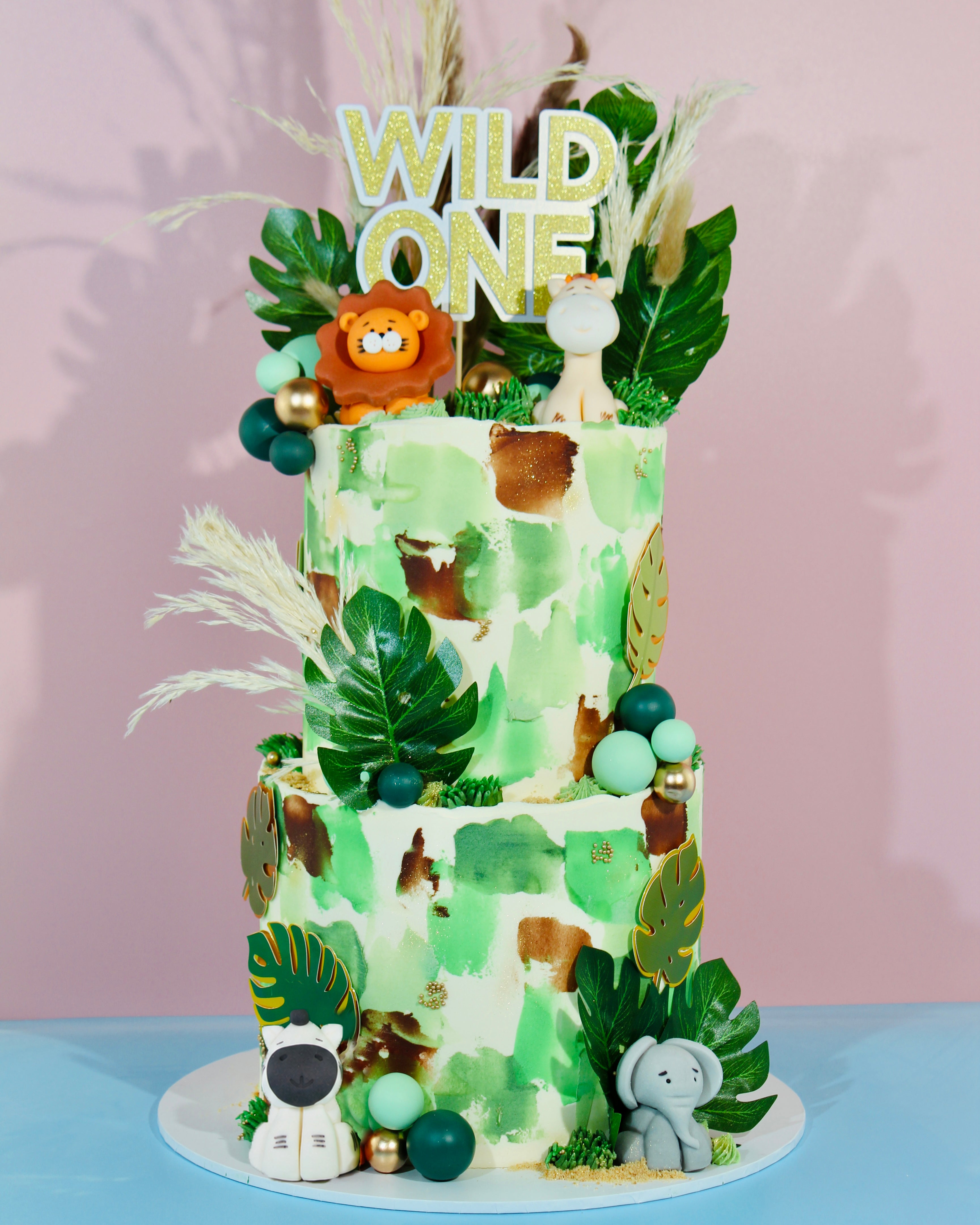Two-tiered birthday cake with jungle theme and 'Wild One' topper
