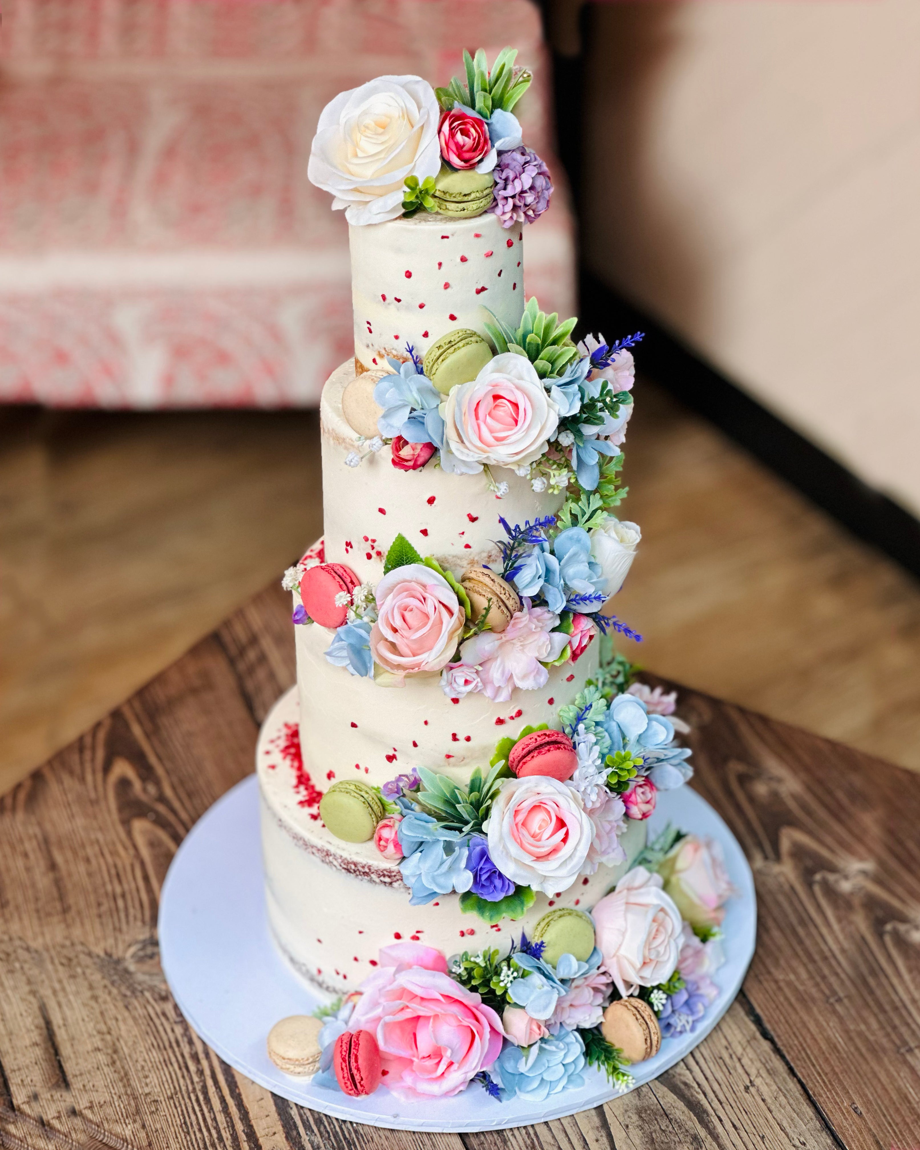 Four-tier wildflower wedding cake with cascading pastel flowers, macarons and semi-naked buttercream finish
