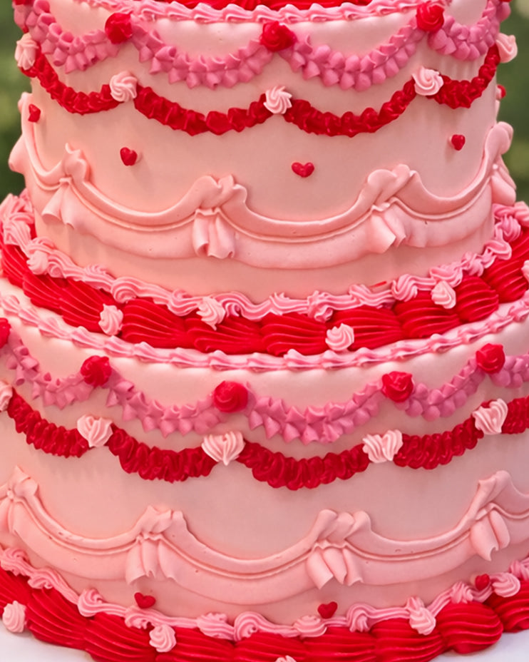Pink and red tiered wedding cake with ornate piping and cherry decoration