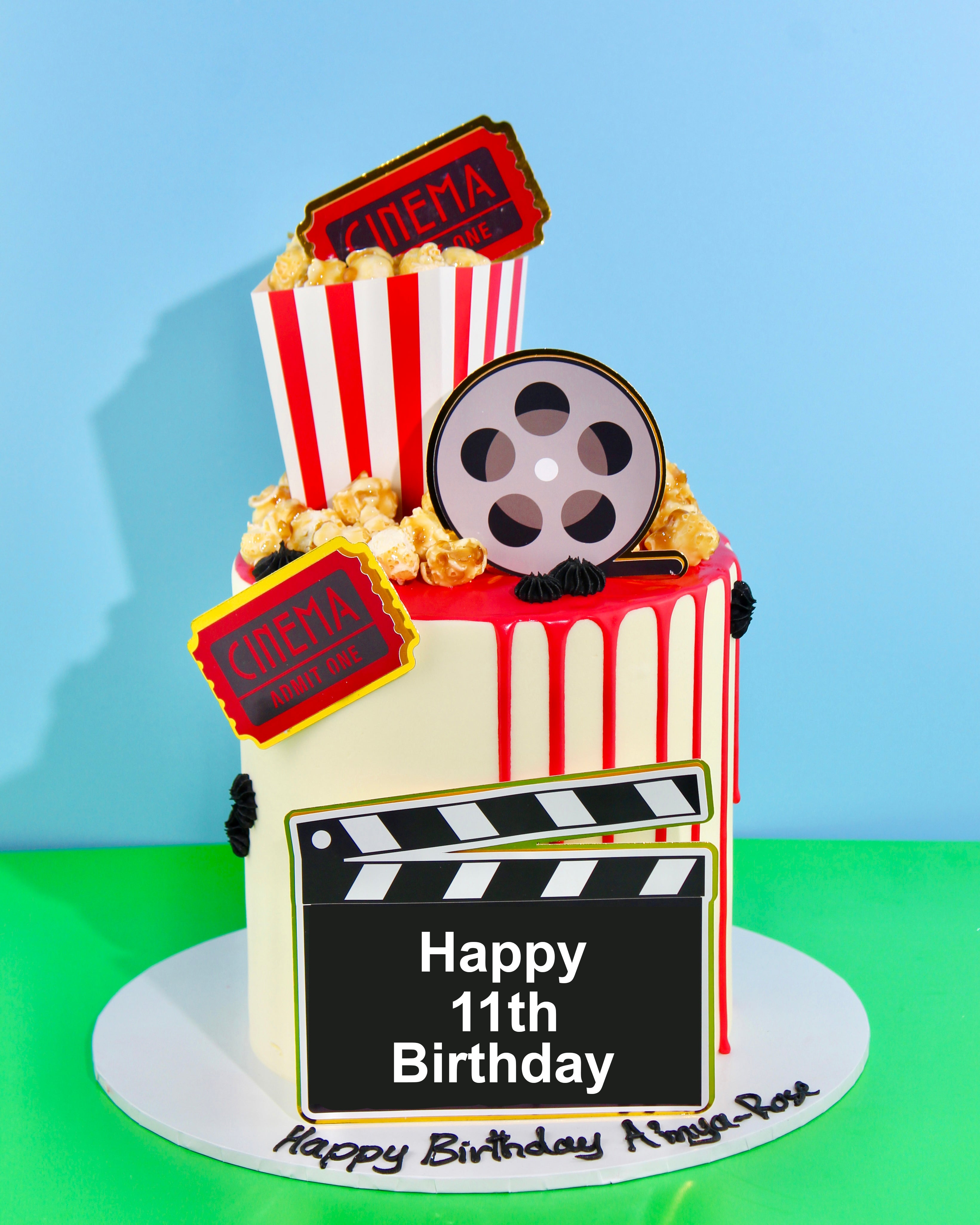 Cinema-themed cake with popcorn box topper, movie tickets, film reel decoration and personalised clapperboard