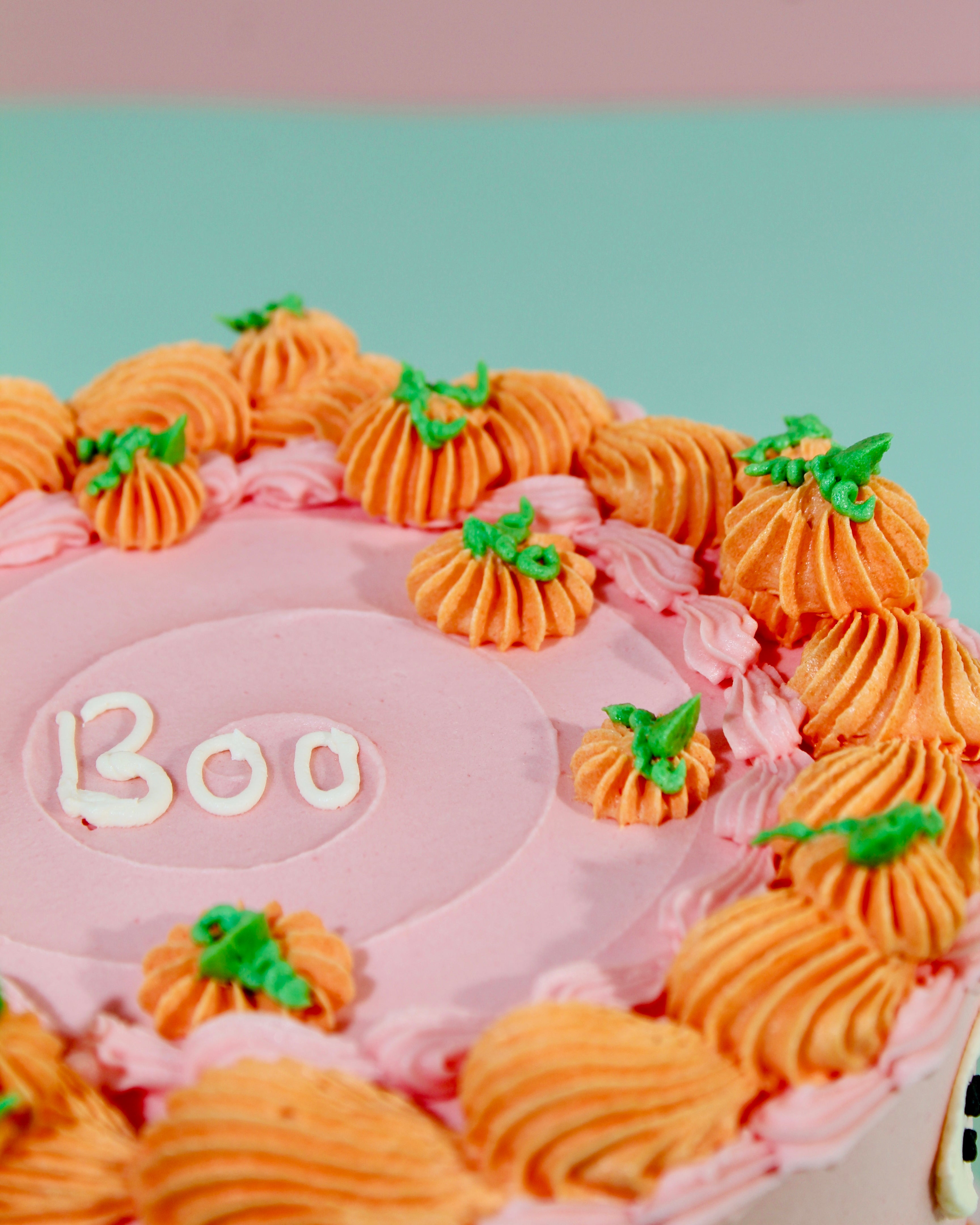 Close-up of white ghost decorations with black dot eyes on smooth pink buttercream Halloween cake sides