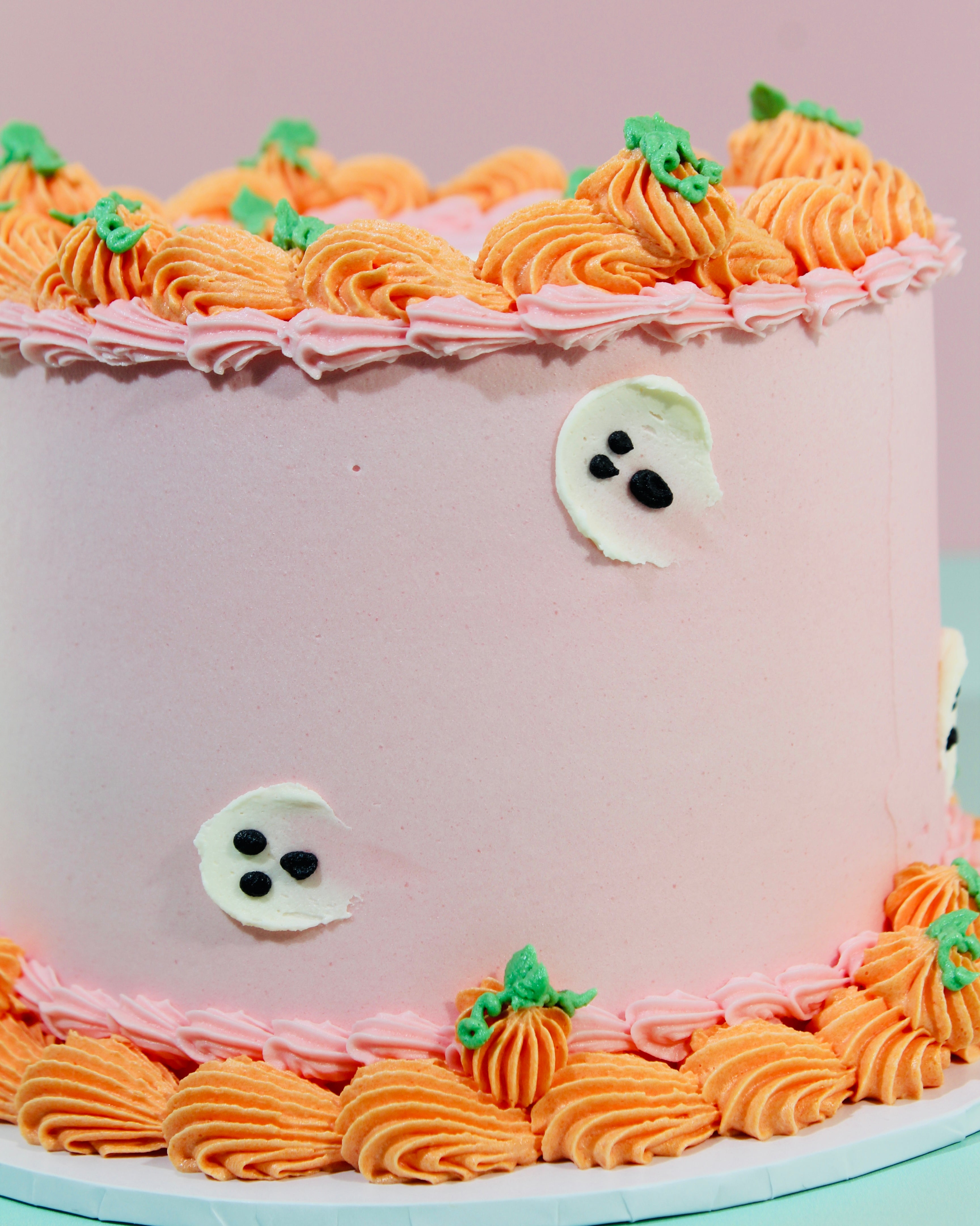 Side view of pink Halloween cake showing orange pumpkin border piping and white ghost decorations on buttercream