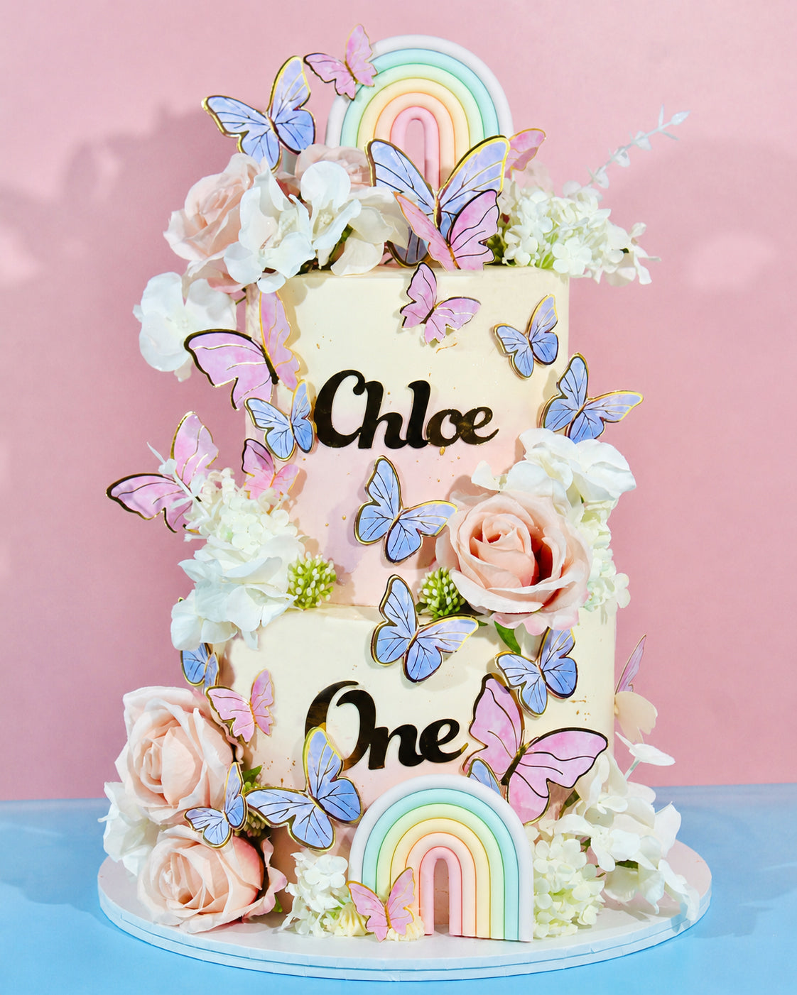 Decorative cake with flowers, butterflies, and rainbow elements on a pink background
