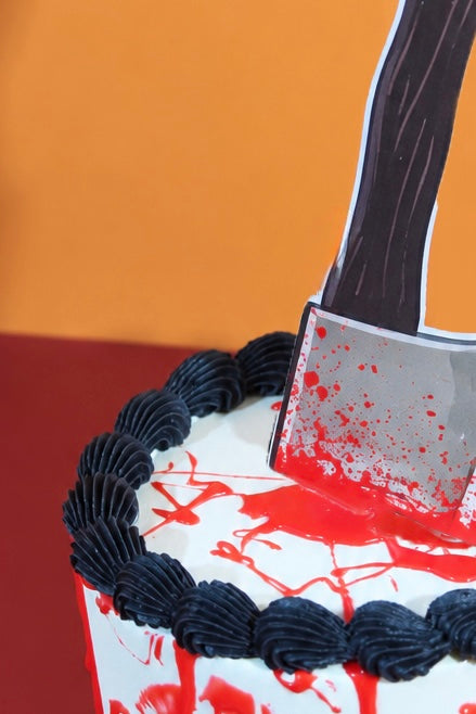 White Halloween cake with red blood splatter drip detail, black buttercream border and cleaver cake topper